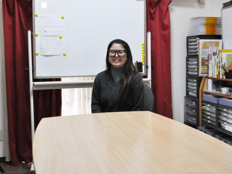 Koga Sensei sitting in front of the whiteboard, at the Fuji Japanese Language School Fukuoka in 2018.